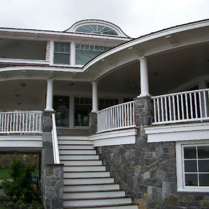 Stone-and-shingle home exterior with wraparound covered porch and curved staircase